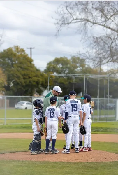 Coach Myles holds a mound meeting with five young baseball players in Long Beach