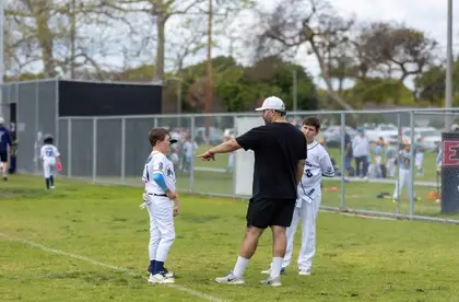 Baseball coach points out fielding positioning to two teen players during practice