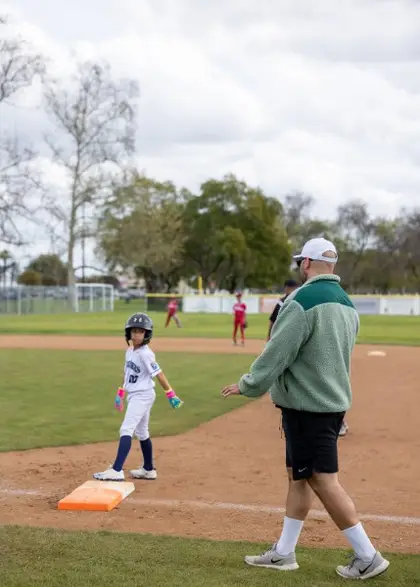 Coach guides a young player on base during an Orange County youth baseball game